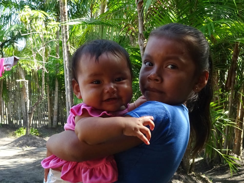 Schattig inheemse meisje die haar baby zusje vasthoudt in Cerros de Mavecure