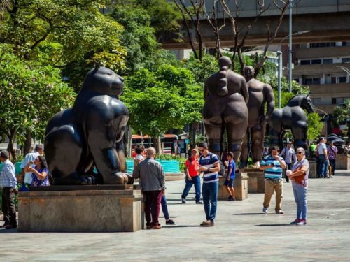 People posing and walking next to Botero statues in center of Medellin