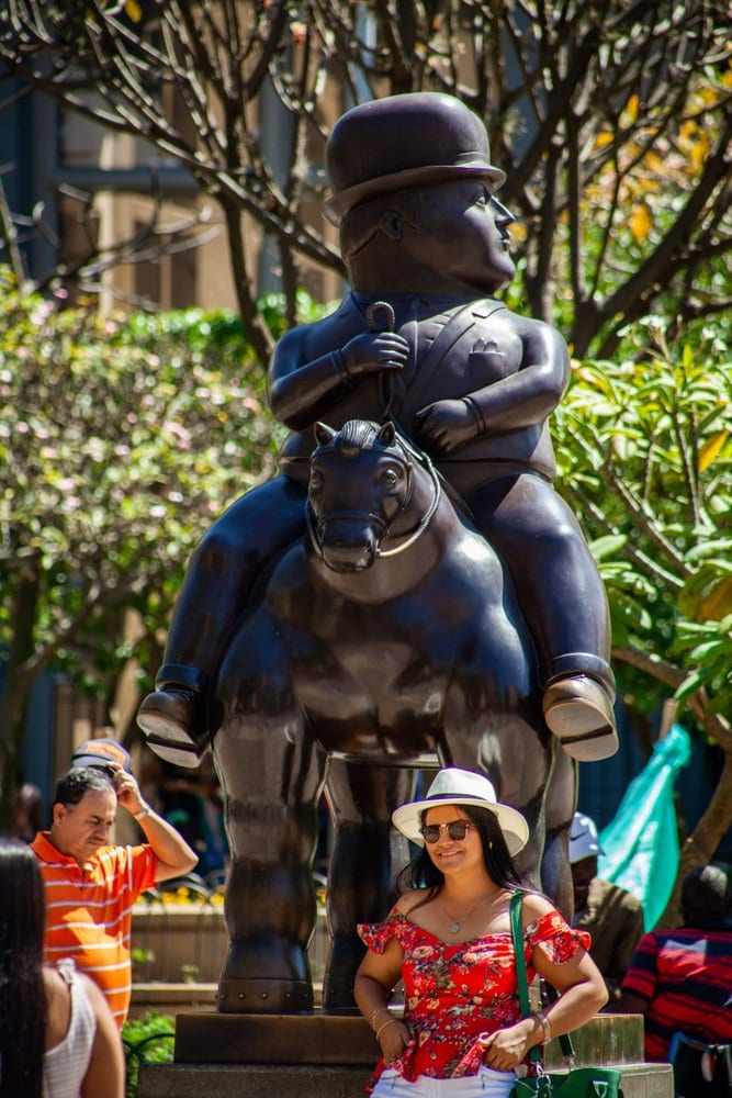 Vrouw poserend voor een standbeeld van een dikke man op een paard van Botero